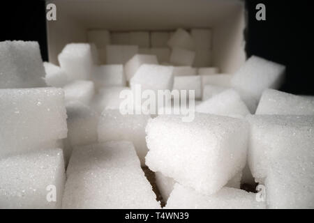 Macro shot di cubetti di zucchero accanto alla scatola di cartone sul tavolo di legno. Cibo malsano dolcificante, dolci cubetti di cristallo Foto Stock