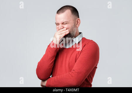 Uomo maturo in maglione rosso ride felicemente a divertente scherzo, essendo di buon umore Foto Stock