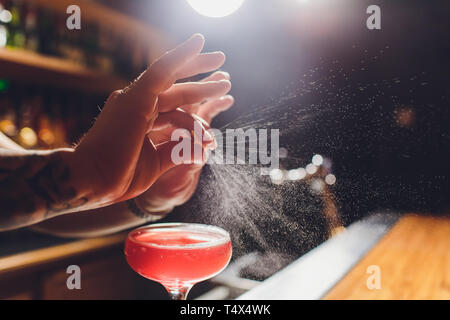 Barman s mani spargendo il succo nel bicchiere da cocktail riempito con la bevanda alcolica su sfondo scuro. Foto Stock
