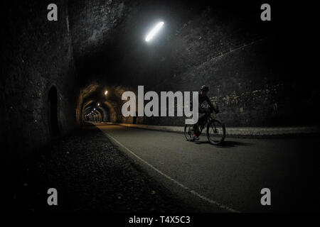 Un uomo che cavalca una bicicletta attraverso un tunnel lungo il sentiero Monsal nel Derbyshire Peak District. Foto Stock