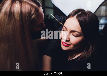 Cosmetologo rendendo le sopracciglia design. Donna attraente getting cura del viso a un salone di bellezza. Architettura perfetta delle sopracciglia. Foto Stock