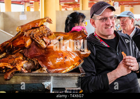 Tourist in posa di fronte di arrosto di maiale interi presso gli agricoltori locali mercato in Ecuador Foto Stock