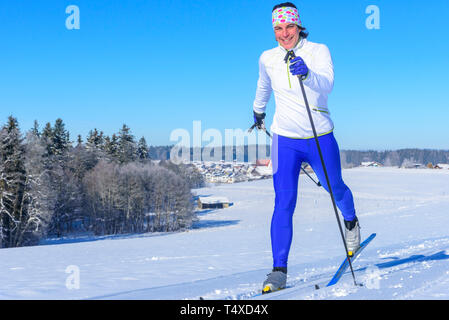 Sciatore femmina facendo cross-paese esercitano su una soleggiata giornata invernale Foto Stock