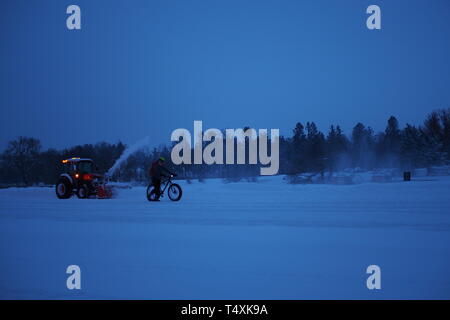 Un ciclista invernale passeggiate passato un trattore la rimozione di neve sul Rideau Canal Skateway presso Dow's Lake, Ottawa, Ontario, Canada. Foto Stock