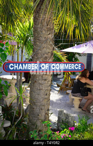 Le persone al di fuori al patio tavolo con ombrellone con un colorato Camera di Commercio segno appeso a un albero di palma in Boca Grande, FL, il Gasparilla Island Foto Stock