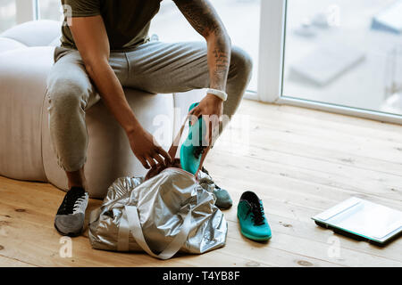 Di carnagione scura sportivo con tattoo mettendo sneakers nel sacco Foto Stock