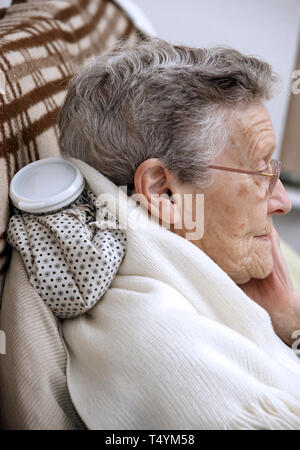 Donna anziana utilizzando un acqua calda la bottiglia per il collo e il dolore alla spalla Foto Stock