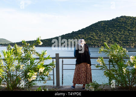 Kas, Turchia - 30 Marzo 2016: Turco donna in usura tradizionale sta cercando il paesaggio con la baia di Kas. Foto Stock