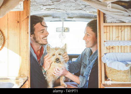 Coppia felice cuddling il loro cane all'interno di una mini van - giovani pronti per un viaggio per divertirsi insieme con il proprio animale Foto Stock