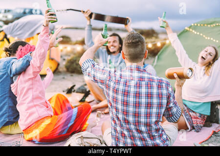 Happy amici facendo parte di bere birre e riproduzione di musica durante il campeggio con le tende per esterno - i giovani per divertirsi e ridere insieme Foto Stock