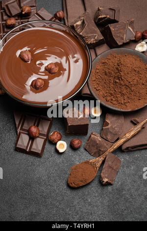 Ciotola di vetro di crema di cioccolato o cioccolato fuso, pezzi di cioccolato e nocciola scuro su sfondo di calcestruzzo Foto Stock