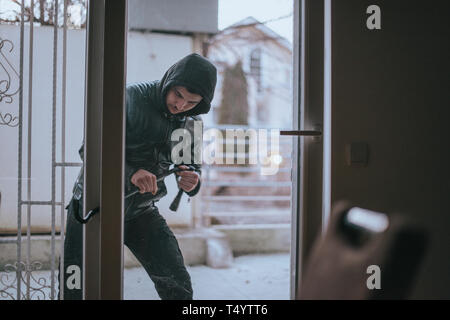 Rapina ragazzo con palanchino cercando di aprire la porta di casa Foto Stock