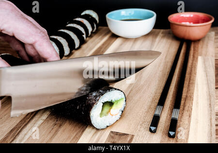 Close-up di persona in casa il taglio di rotoli di sushi con coltello da cucina Foto Stock