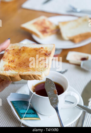 Mano che tiene il pane con marmellata di frutta e la tazza di tè sul tavolo di legno Foto Stock