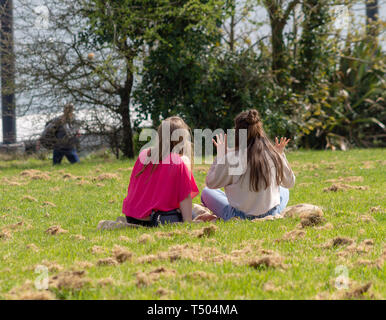 2 giovani donne ragazze sat sul prato di un parco godendo il sole. Foto Stock