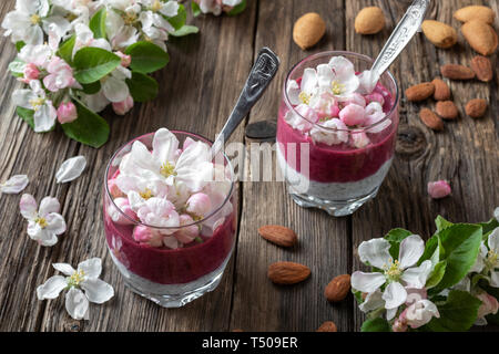 Layered chia il budino con latte di mandorla, yogurt, mirtilli e fiori di Apple Foto Stock