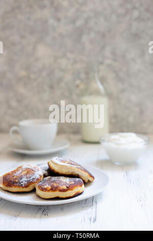 Cottage cheese pancakes, Cheesecake sul tavolo. Syrniki sirniki o. Una sana prima colazione. Piatti bianchi. Bottiglia di latte. Una tazza di latte. Yogurt o sour Foto Stock