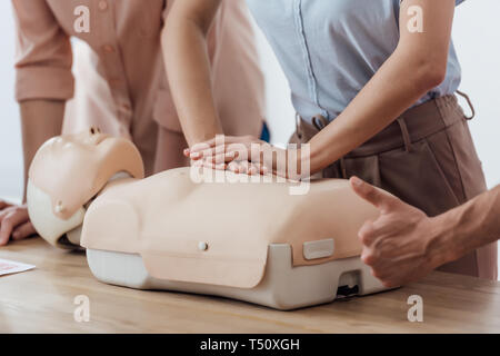 Vista ritagliata della donna di eseguire la compressione toracica su fantoccio durante RCP classe di allenamento mentre l'uomo facendo pollice in alto segno Foto Stock