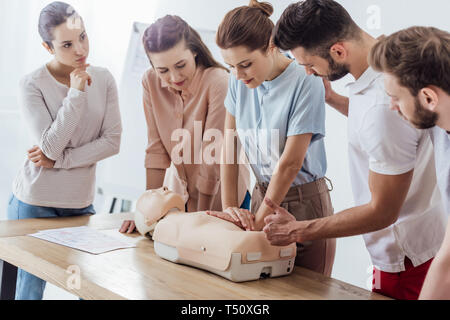 Gruppo di persone focalizzato l'esecuzione della RCP su fantoccio durante la formazione di primo soccorso Foto Stock