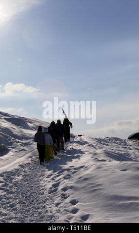 Gli sciatori e gli snowboarder con gli sci e gli snowboard salire sulla strada innevata a inizio inverno mattina. Montagne del Caucaso, Georgia, regione Gudauri. Foto Stock