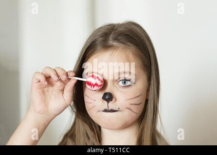 Ragazza bionda con un make-up imitando un gatto che tiene in mano un chupa chups. Foto Stock