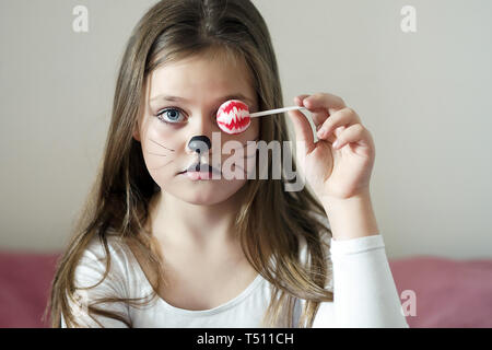 Ragazza bionda con un make-up imitando un gatto che tiene in mano un chupa chups. Foto Stock