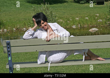 Piuttosto scuro pelose donna seduta su una tavola di legno una panchina nel parco. Foto Stock