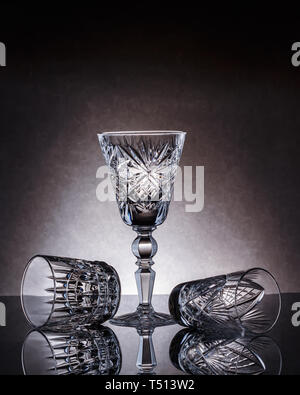 Svuotare bicchieri di cristallo di varie dimensioni su uno sfondo grigio con un riflesso speculare Foto Stock