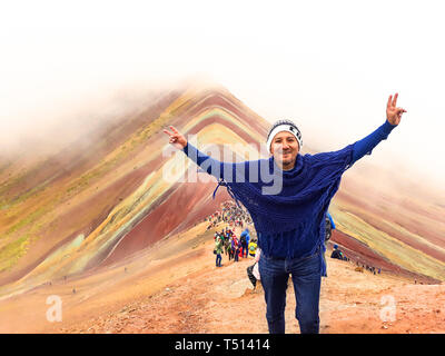 Un giovane maschio tourist godendo la vista delle incredibili montagne Arcobaleno al di fuori della città di Cusco, Perù. Gli importi sono una varietà di colori da depositi minerali nel suolo. Foto Stock