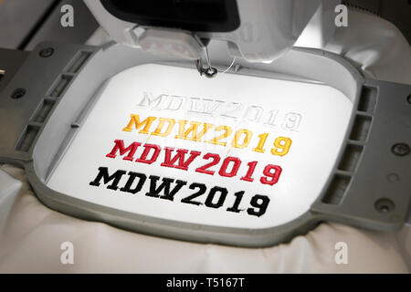 Macchina da ricamo automatica rendendo MDW 2019 segni di diversi colori su tessuto bianco, visualizzato in primo piano Foto Stock