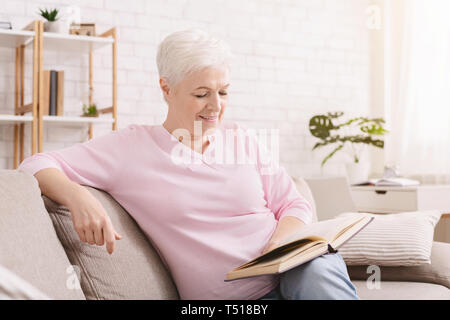 Senior sorridente donna libro di lettura a casa Foto Stock