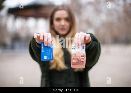 Signora giovane dimostrando la scheda di plastica e contanti alla telecamera rimanendo in posizione di parcheggio Foto Stock