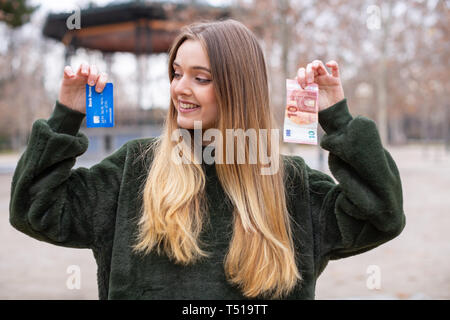 Signora giovane dimostrando la scheda di plastica e contanti alla telecamera rimanendo in posizione di parcheggio Foto Stock