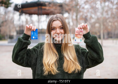 Signora giovane dimostrando la scheda di plastica e contanti alla telecamera rimanendo in posizione di parcheggio Foto Stock