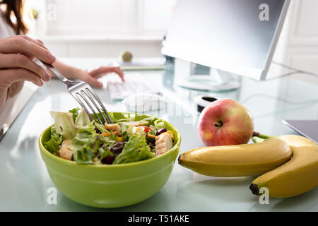 Close-up di donna di mano azienda forcella mentre avente insalata sana sulla scrivania in ufficio Foto Stock