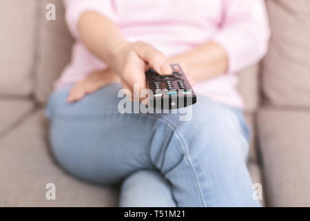 Donna senior di cambiare i canali sul televisore con telecomando Foto Stock