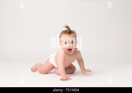 Carino piccolo bimbo in pannolini strisciando sul fondo bianco,immagine luminosa di strisciare curioso baby su bianco backgroubd Foto Stock