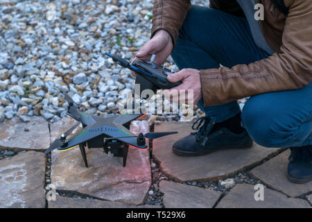 Un uomo si siede vicino al quadcopter con un telecomando nelle sue mani per configurare il dispositivo in serata Foto Stock