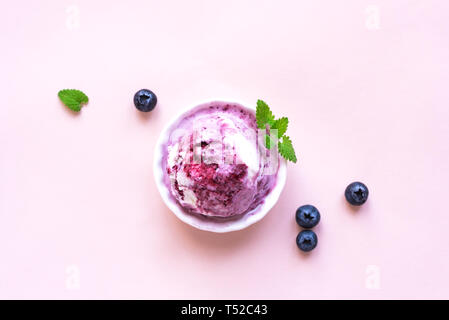 Mirtillo gelati su sfondo rosa, vista dall'alto, copia dello spazio. Convogliatore di gelato in coppa con mirtilli e menta. Foto Stock