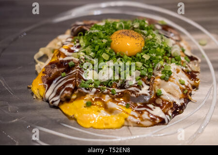 Okonomiyaki, una pizza giapponese / pancake contenenti una varietà di ingredienti, sul pan Foto Stock