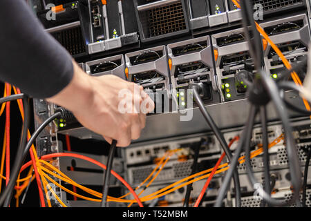 Tecnico maschio collegando il cavo di alimentazione nel pannello in corrispondenza del datacenter Foto Stock