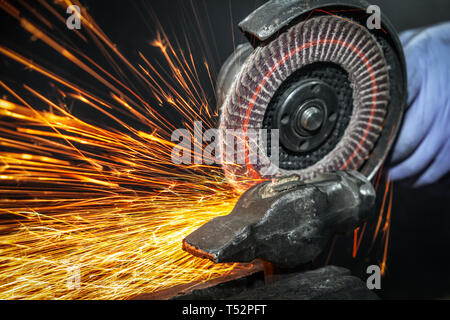 Close-up sui lati volare scintille luminose dall'angolo macchina rettificatrice. Un giovane maschio saldatore in un bianco guanti da lavoro macina un prodotto metallico con angl Foto Stock