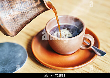 Caffè orientale in stile turco servita nel cezve, un piccolo a lungo gestito la pentola con un beccuccio e cup su una tavola di legno Foto Stock
