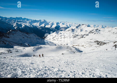 Vista panoramica verso il basso coperto di neve valle nella catena montuosa alpina sul cielo azzurro sfondo con Off-pista sciatori Foto Stock