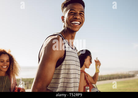 Felice giovane uomo appeso fuori con gli amici in un giorno d'estate. Uomo sorridente e donna amici passeggiate all'aperto con birre. Foto Stock