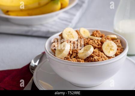 Ciotola di granola witk fette di banana e latte con le banane in background Foto Stock