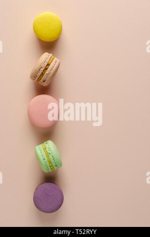 Amaretti multicolore o macarons in una fila sul pastello sfondo beige. Messaggio di saluto o scheda di invito concetto. Verticale. Nessuna dieta giorno Foto Stock