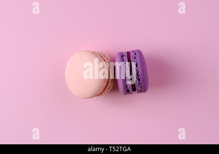 Due dolci dolci francesi di pastello rosa e viola amaretti o macarons sulla rosa pastello sfondo. Spazio per il testo. Messaggio di saluto o un invito del card. Parte superiore Foto Stock