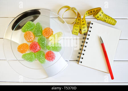 La marmellata di arance sulle scale accanto a un notebook, una penna e un metro a nastro. Il conteggio e la registrazione della quantità di proteina, calorie e grassi negli alimenti. Slim fig Foto Stock