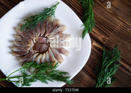 Fette di aringa scandinavo con spezie e aneto in una piastra bianca. Impostazione tabella su un rustico in legno tavolo fatto di tavole di pino Foto Stock